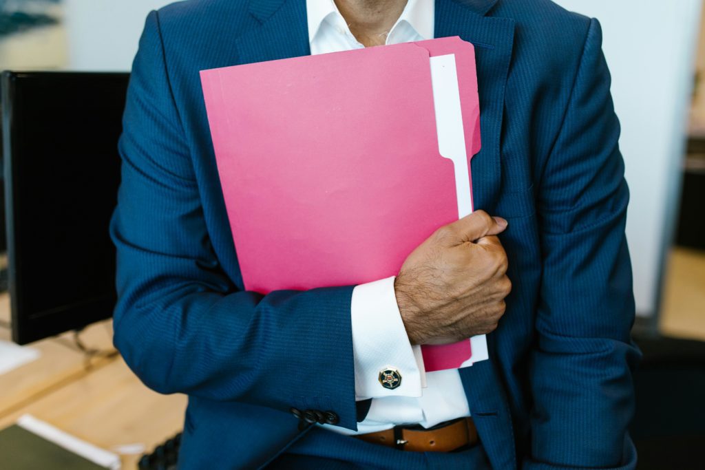 pexels-photo-7580909-7580909 A professionally dressed man holding a pink folder in an office setting.