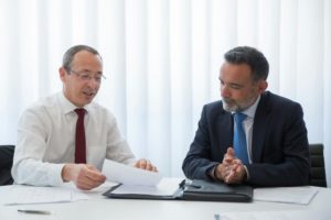 Two businessmen in suits having a discussion over documents in a bright office setting.